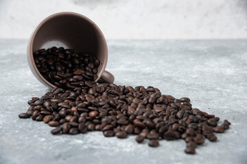 Aromatic roasted coffee beans out of cup on marble surface