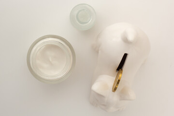 Closeup of a cat-shaped penny bank, facial serum and moisturiser. Concept of affordable skin care.