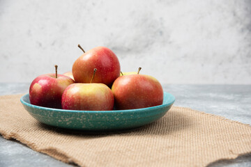 Blue bowl full of fresh apples on marble background