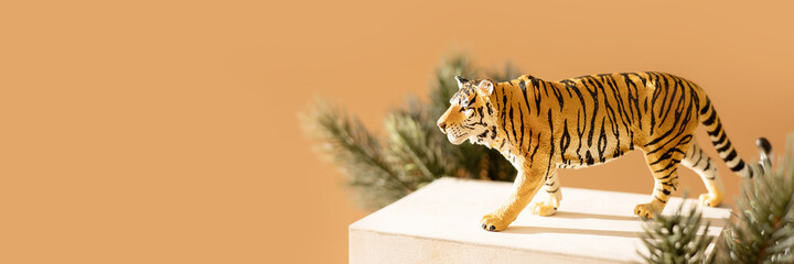 Tiger symbol of the Chinese new year 2022. Figurine of tiger with branches spruce tree on wooden stand on bright background. Copy space. Banner