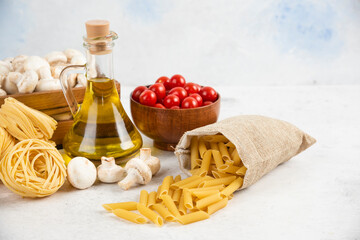 Obraz premium Cherry tomatoes with olive oil, mushrooms and raw pastas on the marble