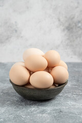 Dark bowl of fresh uncooked eggs on marble background