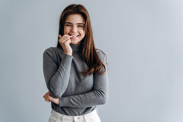 Woman with dark, long hair with happy gentle smile. Cheerful woman on gray background.