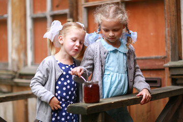 two girls eat jam with a spoon in the yard of the house. Retro. Soviet Union childhood