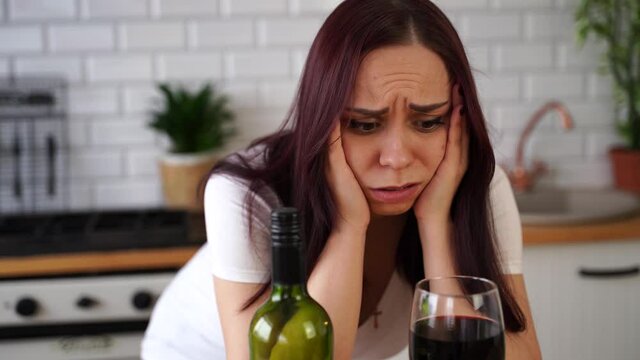Unhappy young woman has headache from red wine. Adult female feels bad from alcohol while in kitchen.