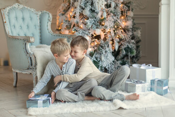 Two little brothers are playing and laughing near the Christmas tree . Family New Year unpacking gifts