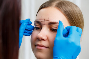 A woman permanent makeup artist draws a sketch of the eyebrows on the face of her client.