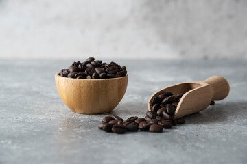 Wooden bowl and spoon of roasted coffee beans on marble background