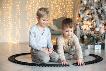 Two cute little boys are playing near the Christmas tree in a red train. Family Christmas and New Year