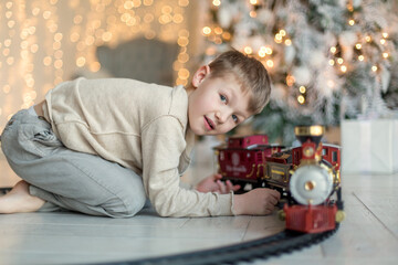 A cute little boy is playing near the Christmas tree in a red train. Family Christmas and New Year