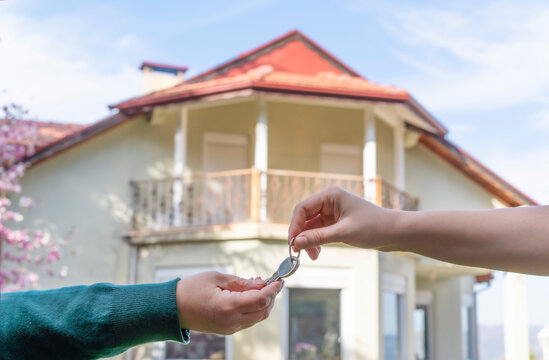 Close Up Of Estate Agent's Hand Give House Key To Buyer's Hand. Person Buy House With Backyard During Coronavirus Pandemic. Concept For Real Estate And Dream House Buying. New Life In First Home.