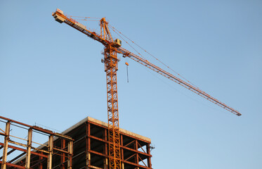 Construction site with lifting crane or turret slewing crane against blue sky on a summer evening with parts of the building (future house) seen.Grow concept 