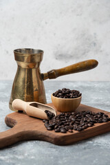 Dark roasted coffee beans and coffee maker on wooden cutting board
