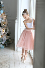 Cute ballerina girl in a full skirt and pointe shoes standing near the Christmas tree