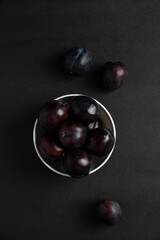 Black plums in white ceramic saucer, top view