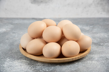 Wooden plate of fresh organic raw eggs on marble surface