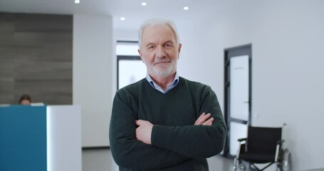 Portrait of confident healthy elderly bearded man, happy senior patient after treatment at clinic crossing arms looking at camera and smiles standing in hospital. Satisfied visitor to medical center