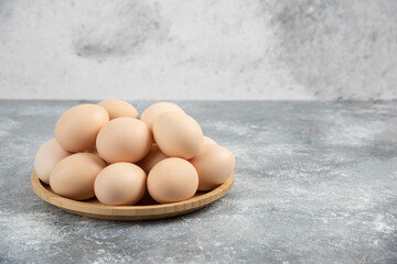Wooden plate of fresh organic raw eggs on marble surface