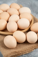 Wooden plate of organic uncooked eggs on marble surface