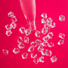 Bottled water spilled on a glass table. Pieces of ice in water and a neck in a bottle on a red background