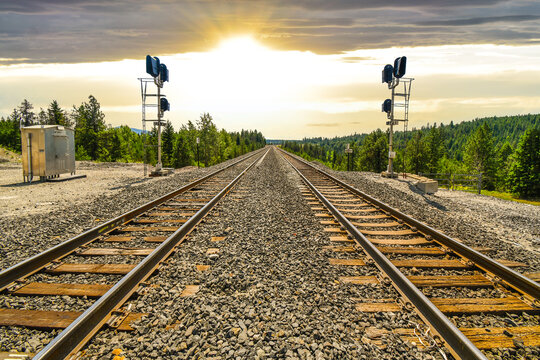 A long set of railroad train tracks disappear as the sun sets in the distance through the mountains in the rural area of North Idaho.