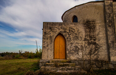 Obraz premium Puerta trasera de madera con arco gótico puntiagudo de una iglesia abandonada en un entorno rural