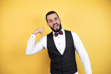Young man with beard wearing bow tie and vest smiling doing phone gesture with hand and fingers like talking on the telephone