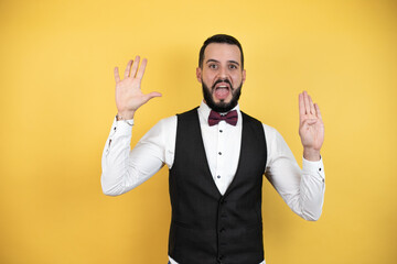 Young man with beard wearing bow tie and vest showing and pointing up with fingers number nine while smiling confident and happy