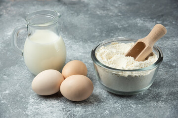 Flour, raw eggs and milk on marble background