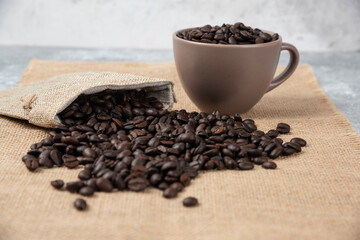 Bunch of medium roasted coffee beans out of sackcloth on marble surface