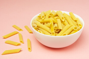 Penne italian pasta in white ceramical bowl on pink background with copy space.