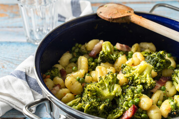 Top view on fresh prepared broccoli with gnocchi in casserole dish on the wooden table - homemade healthy food in bright light with copy space