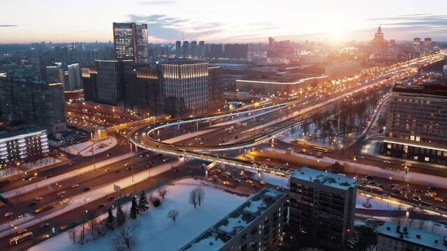 View from above to Moscow multi-level highway in winter lit by the sunset light. Camera showing panorama of the evining city and then coming closer to the junction with a lot of traffic.