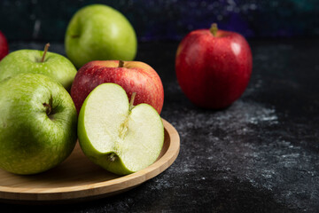 Whole and sliced green and red apples on wooden plate