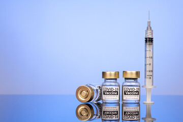 Covid-19 vaccine vial with syringe concept on reflective surface on blue background