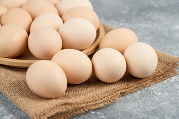Wooden plate of organic uncooked eggs on marble surface