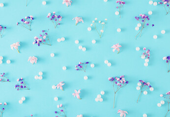 Beautiful nature concept made of colorful flowers and pearls on pastel blue background. Spring or summer pattern. Flat lay.