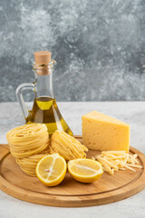 Wooden board of spaghetti nests, oil, lemon and cheese on white table