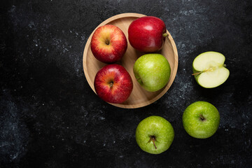Whole and sliced green and red apples on wooden plate