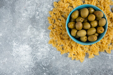 Uncooked farfalle and bowl of olives on marble background