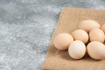 Raw organic eggs placed on top of sackcloth on marble background