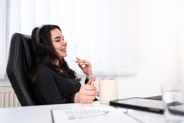 Happy beautiful young girl listening to music while taking a break at the office.