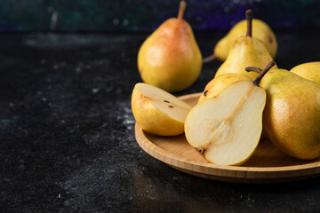 Naklejka na ściany i meble Wooden plate of delicious yellow pears on black surface