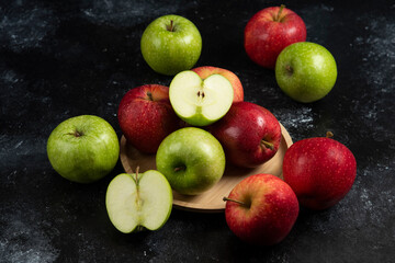 Whole and sliced green and red apples on wooden plate
