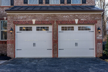 White electronic garage doors with metal steel spade hinge light red brick siding on a two single space garage new construction luxury American single family home in the East Coast USA © tamas