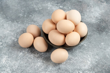 Dark bowl of fresh uncooked eggs on marble background