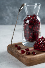 A glass pitcher full of fresh pomegranate and spoon
