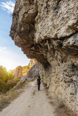 Lonely man, tourist or hiker walking on a pathway under the rock formation, view from behind. 