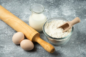 Flour, eggs, milk and rolling pin on marble surface