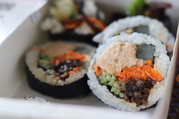 a close up of several kimbap in white paper lunch box which contain of white rice tuna carrot cucumber burdock and pickled radish
